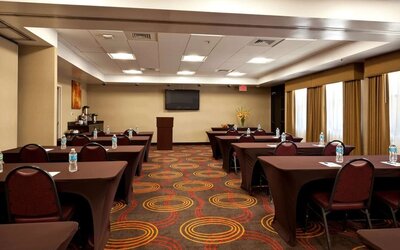 Meeting area arranged with tables and chairs, water bottles, a presentation screen, a podium, and large curtained windows at Best Western Plus BWI Airport Arundel Mills.
