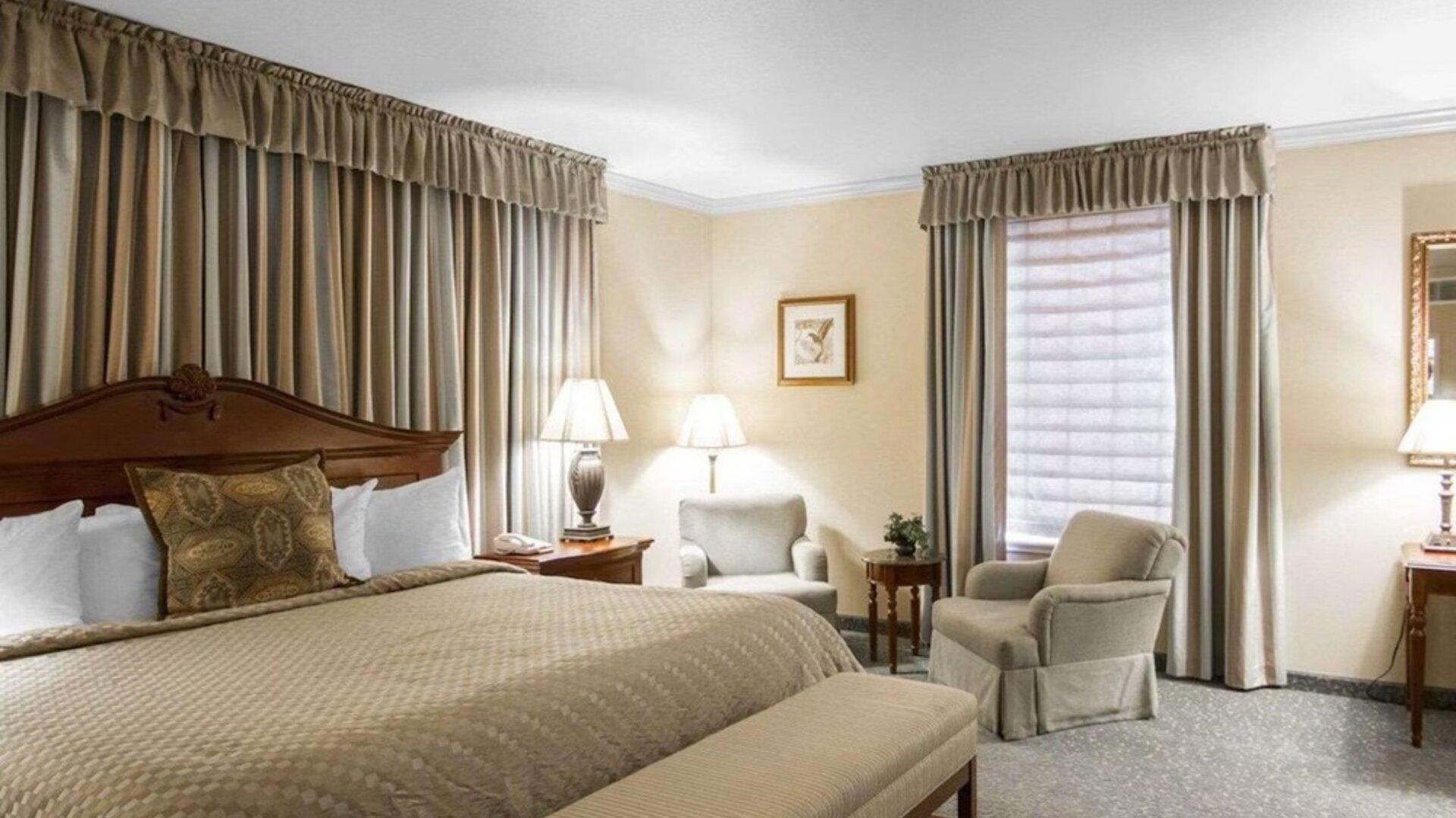 Spacious king guest room with a large wooden bed, beige bedding, upholstered seating, a round coffee table, framed artwork, and a separate desk area at Liberty Hotel Cleburne, an Ascend Hotel Collection Member.