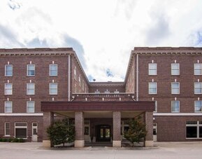 Exterior view of Liberty Hotel Cleburne, showcasing its multi-story red-brick architecture, symmetrical windows, covered main entrance, and landscaped frontage.