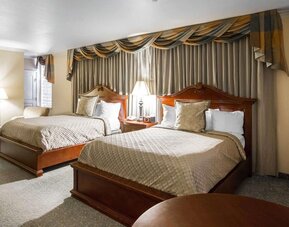 Guest room with two beds, beige patterned bedding, wooden headboards, matching bedside tables, decorative curtains, and a comfortable seating area at Liberty Hotel Cleburne, an Ascend Hotel Collection Member.