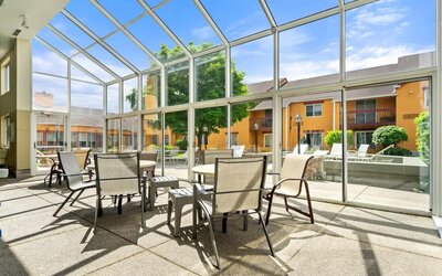 Bright indoor courtyard seating area with floor-to-ceiling glass windows, tables and chairs, and views of the hotel's landscaped courtyard and outdoor pool area at Chicago Club Inn & Suites.