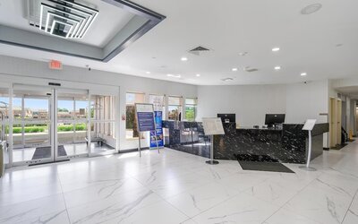 Hotel reception area featuring a black marble-patterned front desk, computer workstations, glass entrance doors, and a bright tiled lobby at Chicago Club Inn & Suites.