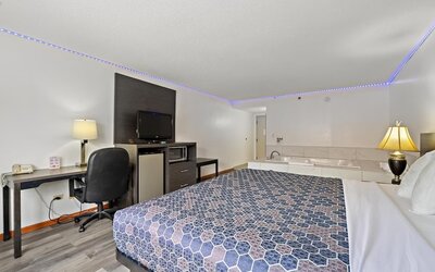Guest room featuring a king-size bed with a blue geometric-patterned bedspread, a dark wood headboard, a desk, a sofa, and a private in-room whirlpool tub at Chicago Club Inn & Suites.
