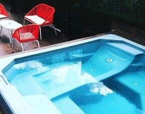 An outdoor swimming pool with built-in seating and clear blue water, surrounded by a wooden deck and red outdoor chairs at Residencial & Hotel Palazzo.