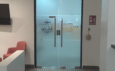 A reception area with frosted glass double doors, a wall-mounted television, coral chairs and a dark countertop at Residencial & Hotel Palazzo.