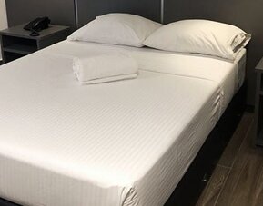 A double bed with white linens and folded towels, dark bedside tables and a black headboard against a dark accent wall at Residencial & Hotel Palazzo.