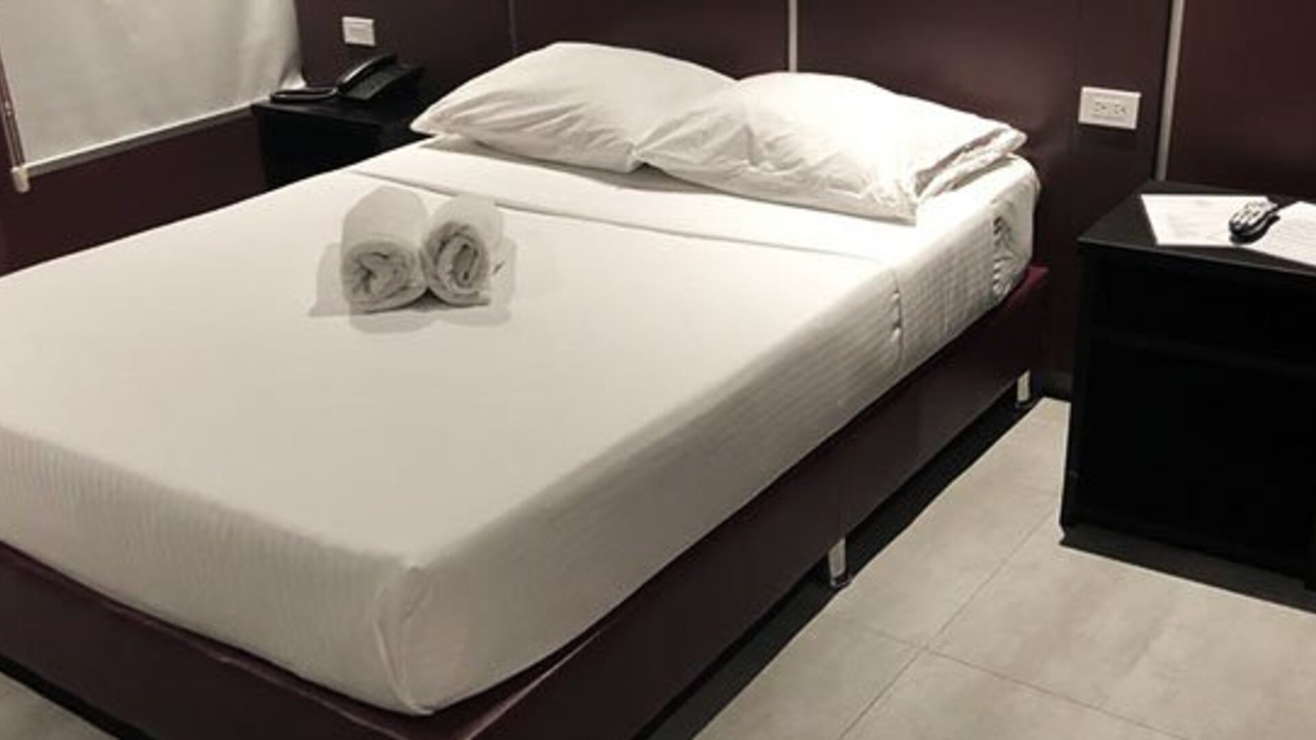 A double bed with white linens and rolled towels, dark bedside tables and wood-look flooring at Residencial & Hotel Palazzo.