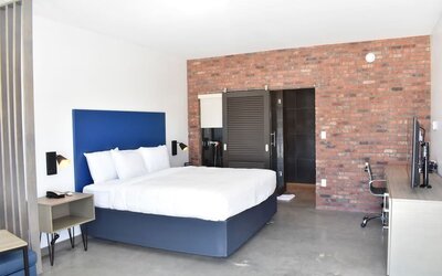 A spacious guest room with a king bed, white linens, a blue upholstered headboard, exposed brick accent wall, desk and office chair at Hotel Bella.
