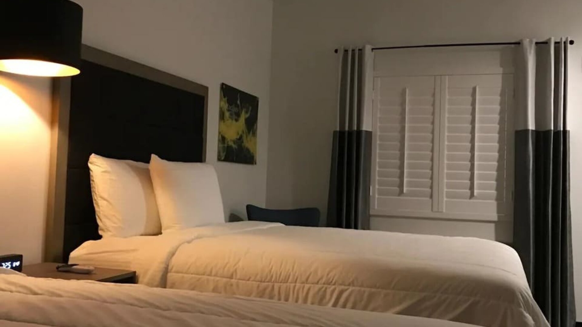 A spacious guest room with two beds, white linens, dark bed frames, a television and a compact kitchenette with white cabinetry at Hotel Bella.