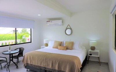 A spacious guest room with a king-size bed dressed in white linens and a beige throw, decorative cushions, matching bedside tables, woven lamps and a small outdoor seating area beside the window at Mucura Hotel And Spa.
