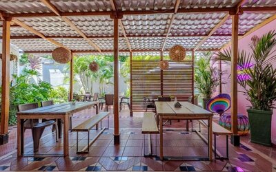 A covered outdoor dining area with wooden tables and benches, woven pendant lights, tropical plants and colourful decorative accents at Mucura Hotel And Spa.