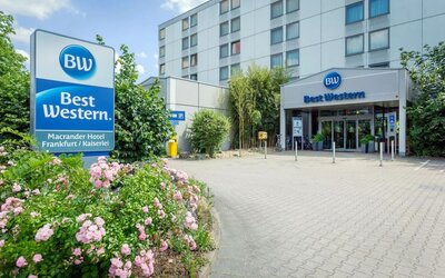 The exterior of Best Western Macrander Hotel Frankfurt/Kaiserlei, showcasing its multi-storey modern building, clearly branded entrance, paved forecourt, parking area and landscaped flower beds.