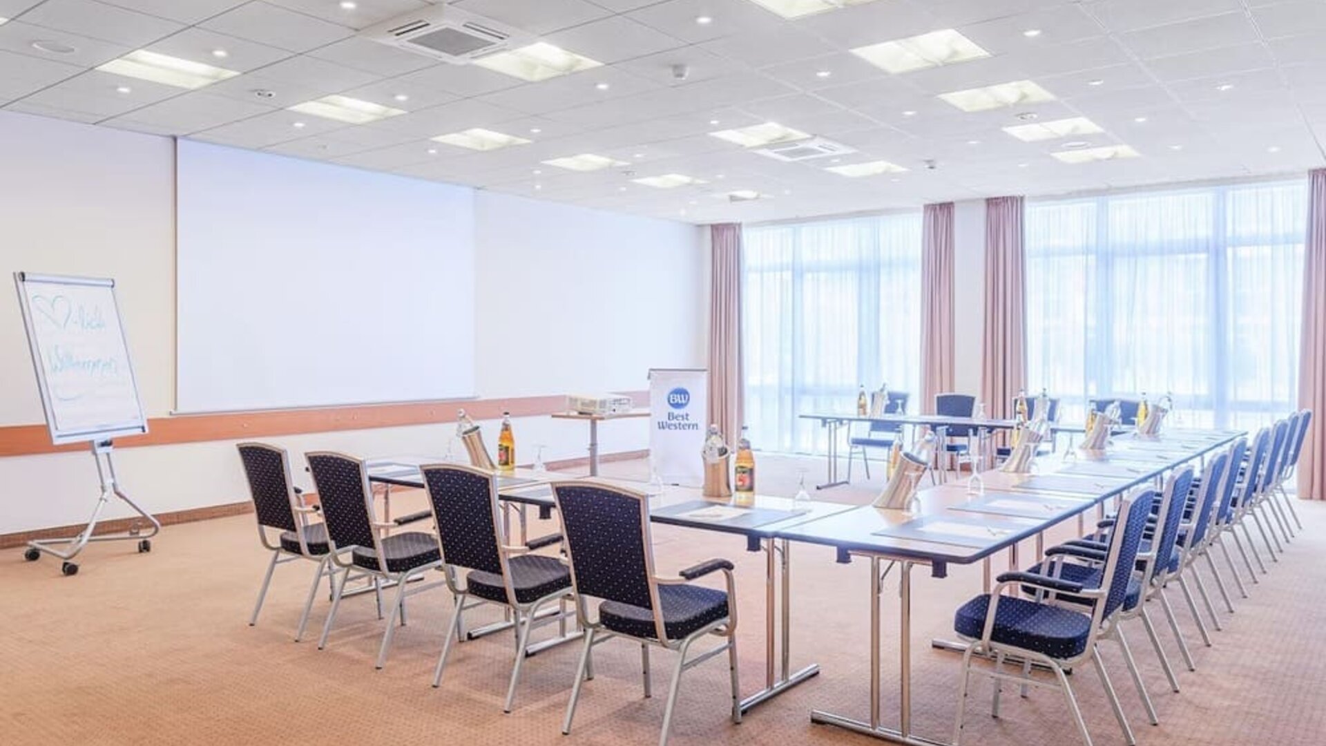 A meeting room configured in a boardroom-style layout, with tables arranged in a rectangular formation, conference chairs, presentation equipment, a flip chart and large windows providing natural light.A recreational area featuring a black foosball table 