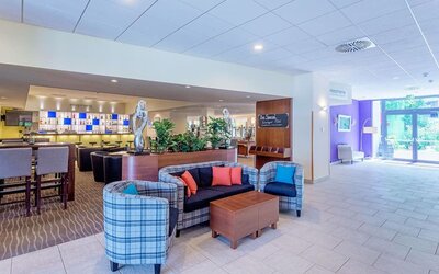 The hotel lobby lounge, featuring a comfortable seating arrangement with plaid armchairs, a sofa with colourful cushions, wooden coffee tables, decorative sculptures and an adjacent bar area.