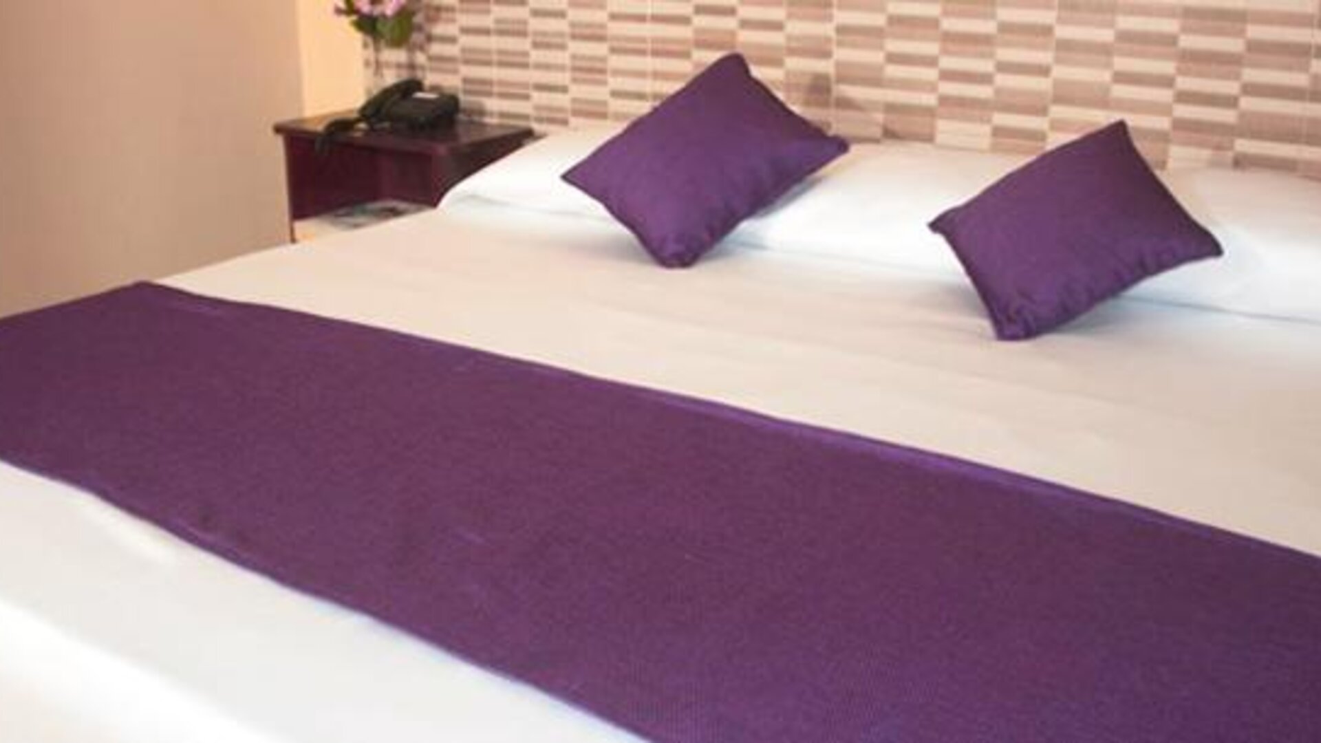 White bed with purple cushions and a matching bed runner against a patterned headboard at Caribe Panamá Hotel.