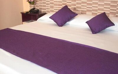 White bed with purple cushions and a matching bed runner against a patterned headboard at Caribe Panamá Hotel.