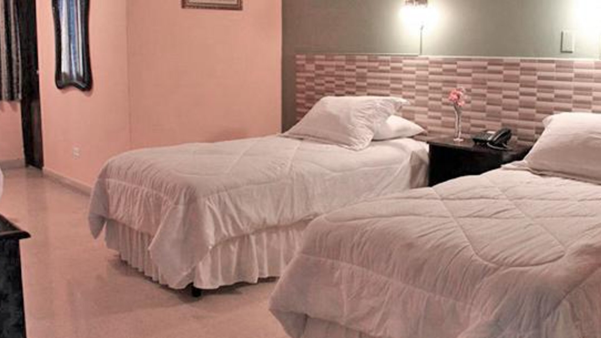 Two single beds with white bedding, a patterned headboard wall and dark curtains at Caribe Panamá Hotel.
