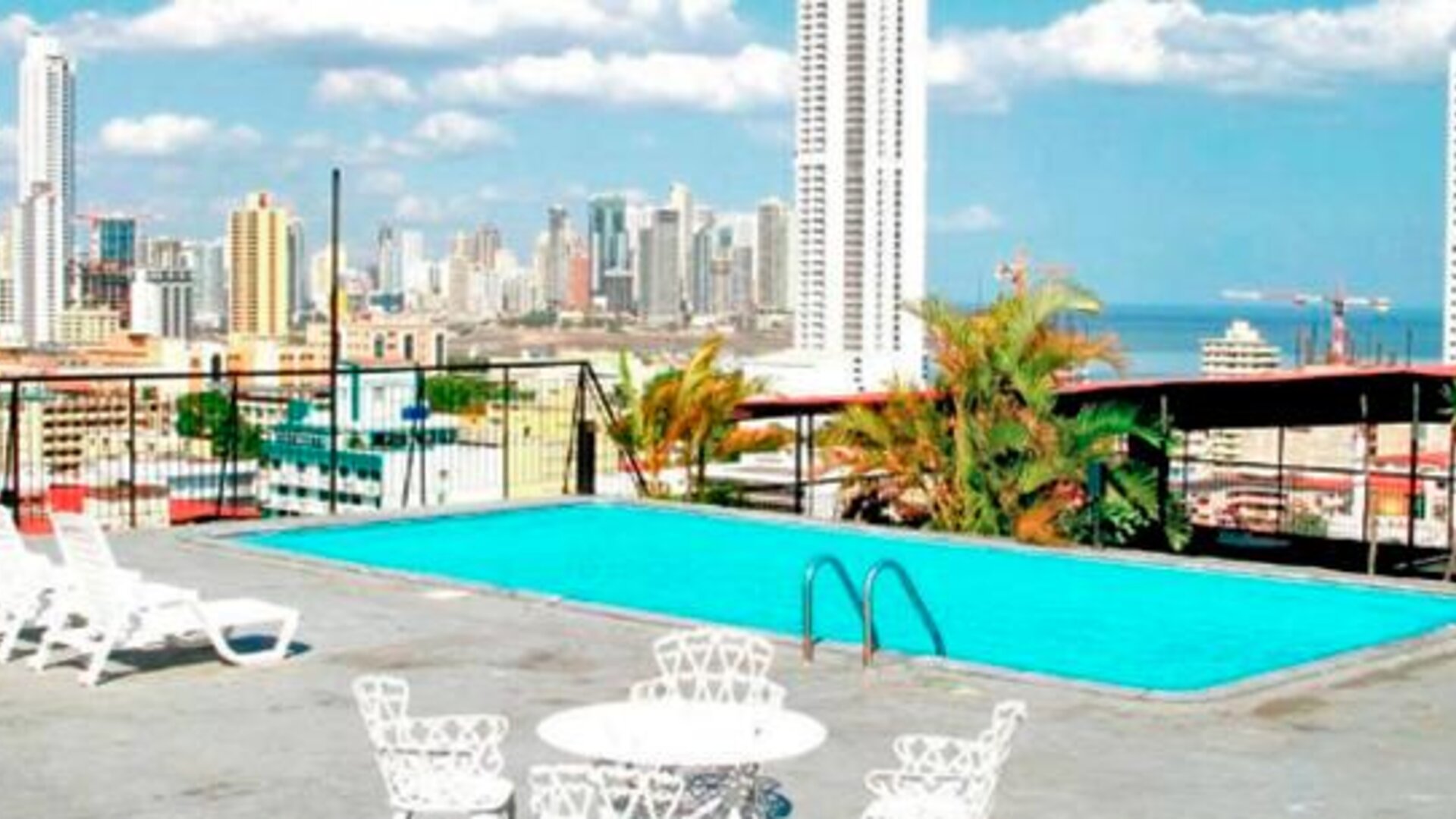 Rooftop swimming pool with white loungers and views of Panama City's skyline and ocean at Caribe Panamá Hotel.