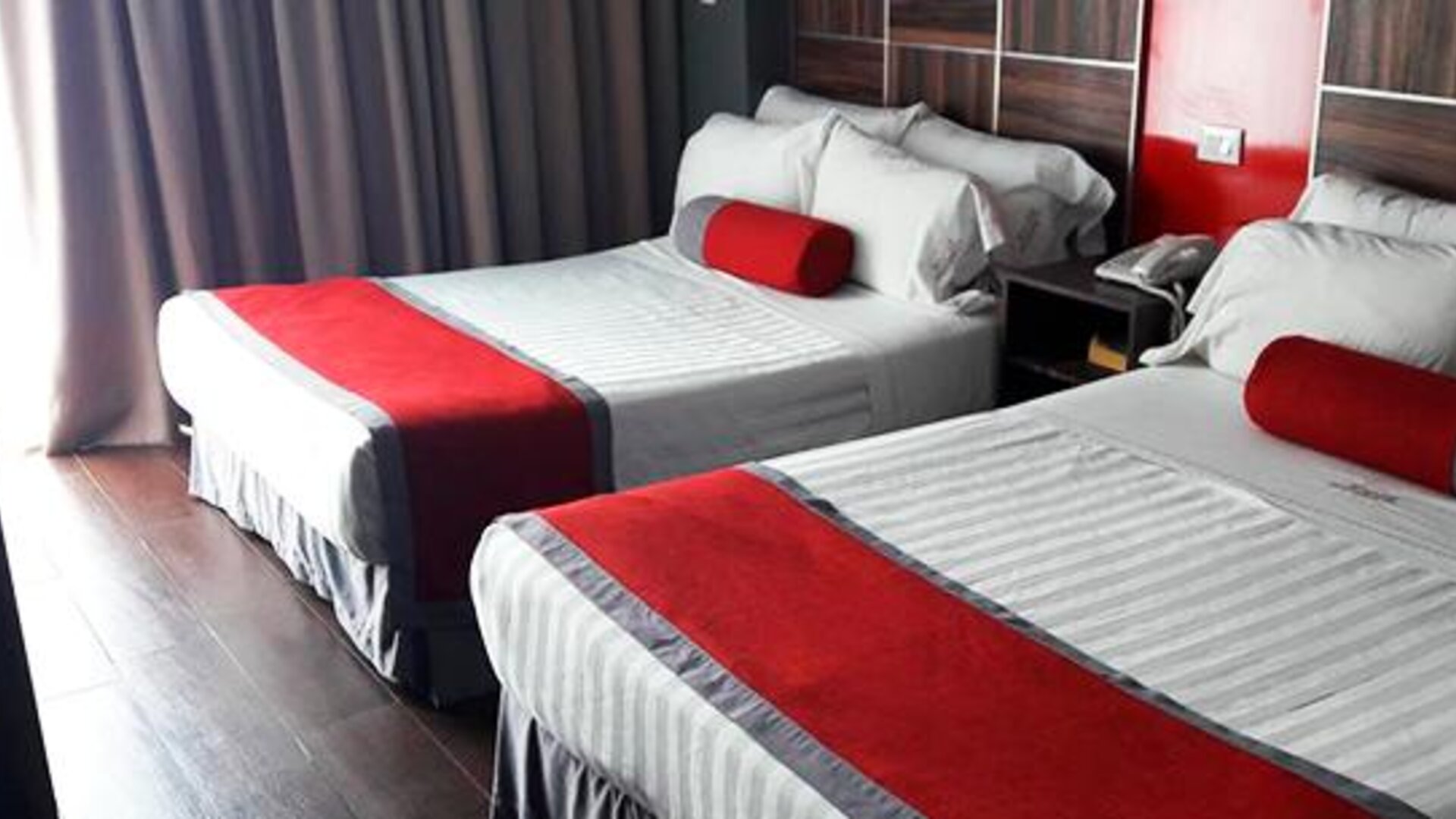 Guest room with two beds featuring white striped bedding, red runners and cushions, dark wood headboards and floor-to-ceiling curtains at Hotel Block Suites.