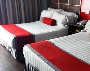 Guest room with two beds featuring white striped bedding, red runners and cushions, dark wood headboards and floor-to-ceiling curtains at Hotel Block Suites.