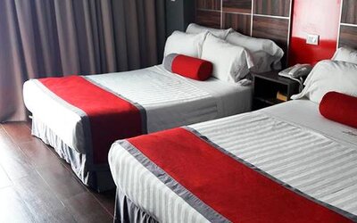 Guest room with two beds featuring white striped bedding, red runners and cushions, dark wood headboards and floor-to-ceiling curtains at Hotel Block Suites.