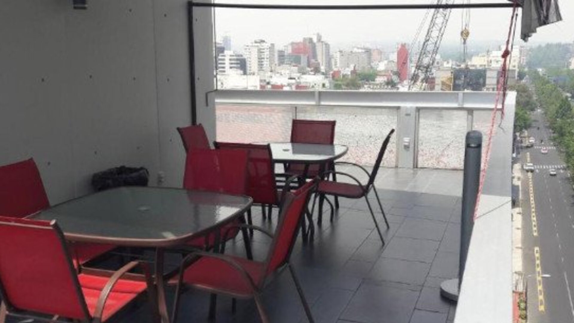 Outdoor terrace with tables and red chairs, glass railing and elevated views of the surrounding city at Hotel Block Suites.