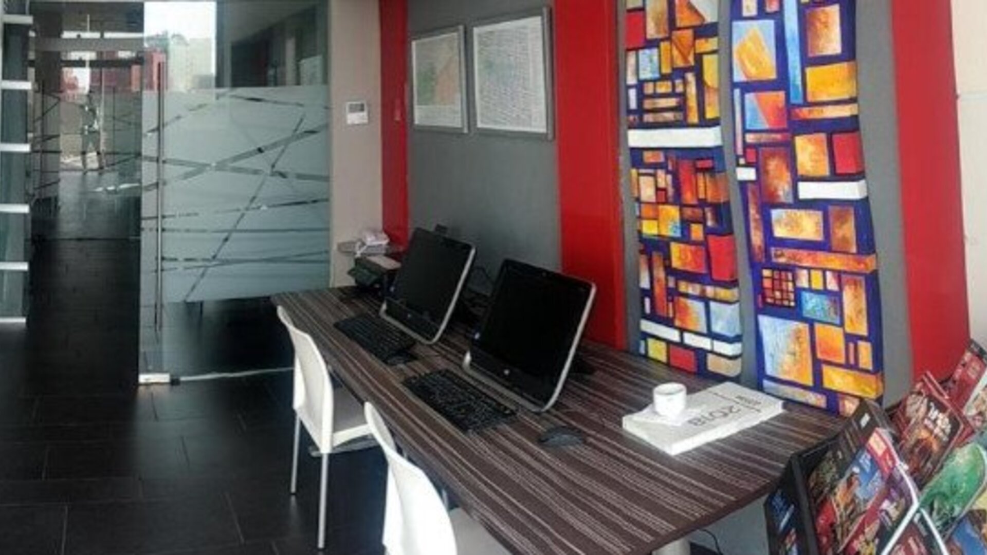 Business centre with computer workstations, white chairs, colourful decorative panels and a dark tiled floor at Hotel Block Suites.