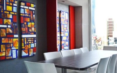 Meeting room with a long conference table, white chairs, colourful geometric wall art and large windows overlooking the city at Hotel Block Suites.