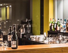 Hotel bar with wine bottles, glassware, a wooden counter and illuminated shelving at Howard Johnson Plaza Buenos Aires.