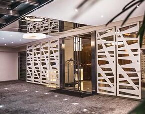 Hotel entrance with glass doors, white geometric screens, dark stone flooring and potted plants at Howard Johnson Plaza Buenos Aires.
