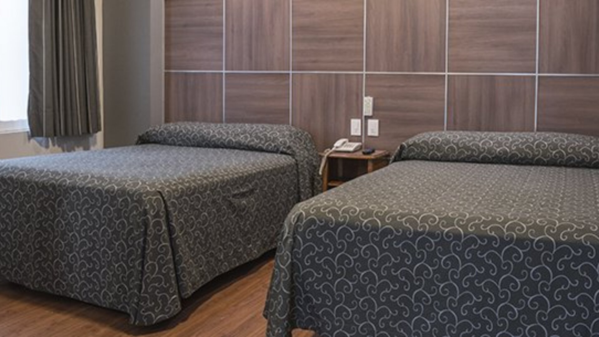 Guest room with two single beds, patterned dark bedspreads and a wood-panelled headboard at Hotel Principal.
