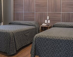 Guest room with two single beds, patterned dark bedspreads and a wood-panelled headboard at Hotel Principal.