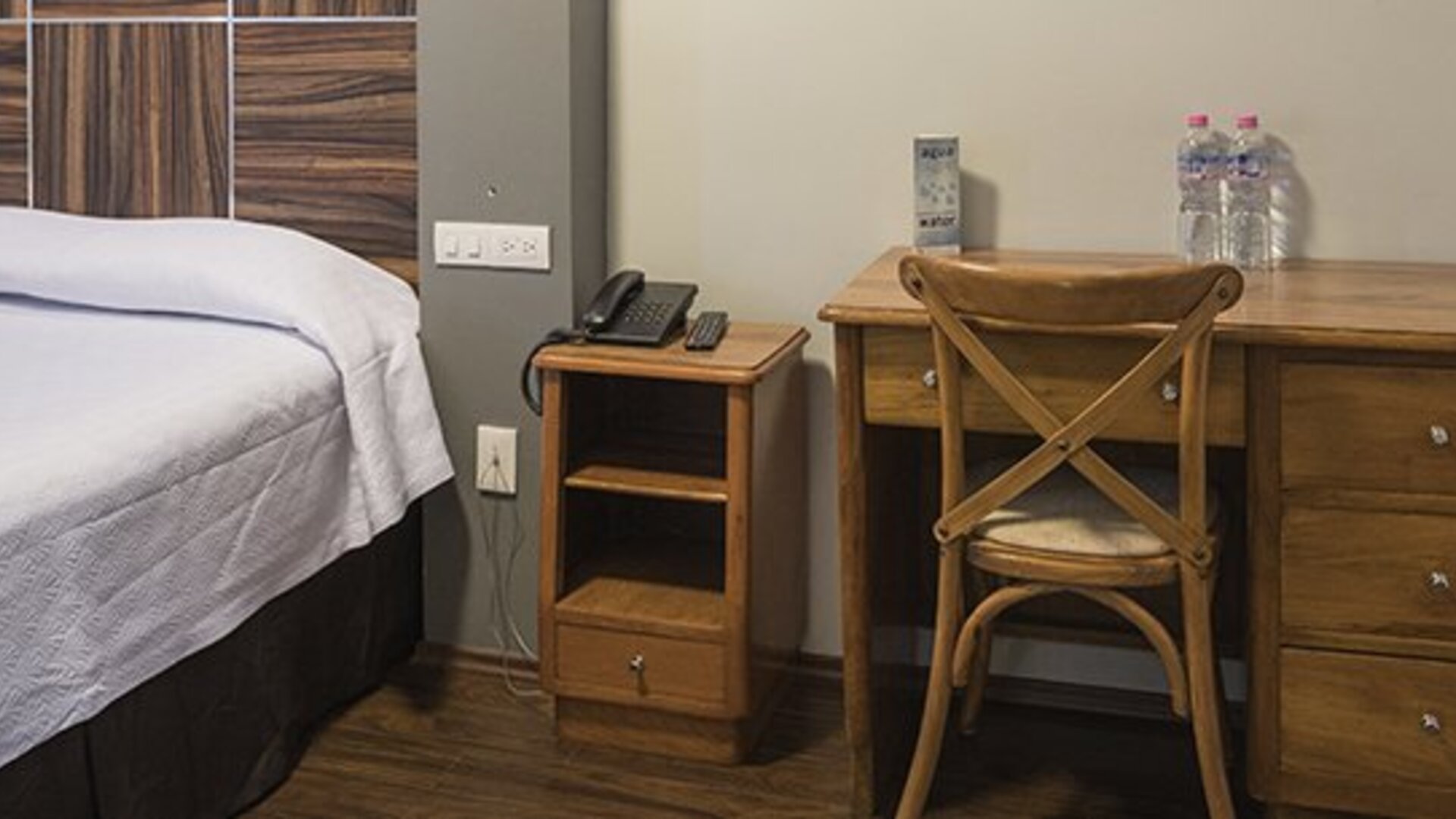 Guest room with a bed, wooden headboard, bedside table, telephone and desk with bottled water at Hotel Principal.