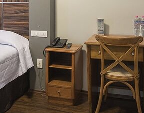 Guest room with a bed, wooden headboard, bedside table, telephone and desk with bottled water at Hotel Principal.