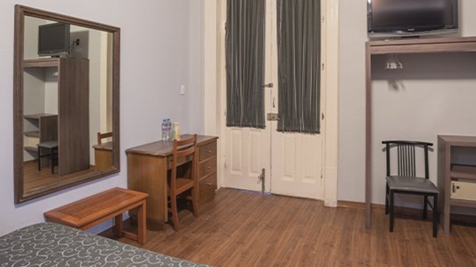 Work area with a wooden desk, chair, wall-mounted television and large mirror at Hotel Principal.