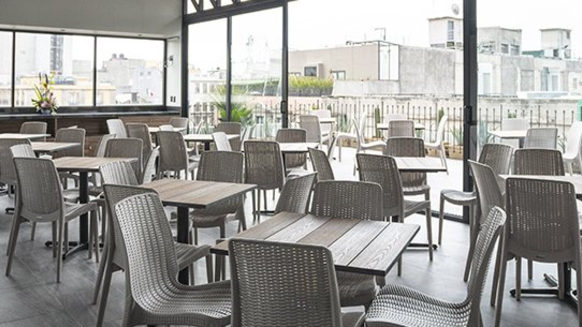 Indoor dining area with square tables, grey woven chairs and floor-to-ceiling windows at Hotel Principal.