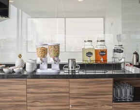 Breakfast beverage station with cereal dispensers, juice dispensers, coffee equipment, cups and glassware at Hotel Principal.
