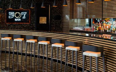 Bar 507 with a long counter, striped decorative panels, pendant lighting and bar stools at Hotel Las Américas Golden Tower Panamá.