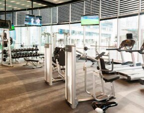 Fitness centre with treadmills, weight machines, dumbbells and large windows overlooking the city at Hotel Las Américas Golden Tower Panamá.