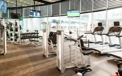 Fitness centre with treadmills, weight machines, dumbbells and large windows overlooking the city at Hotel Las Américas Golden Tower Panamá.