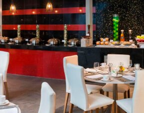 Restaurant dining area with white upholstered chairs, set tables and a buffet counter at Hotel Las Américas Golden Tower Panamá.