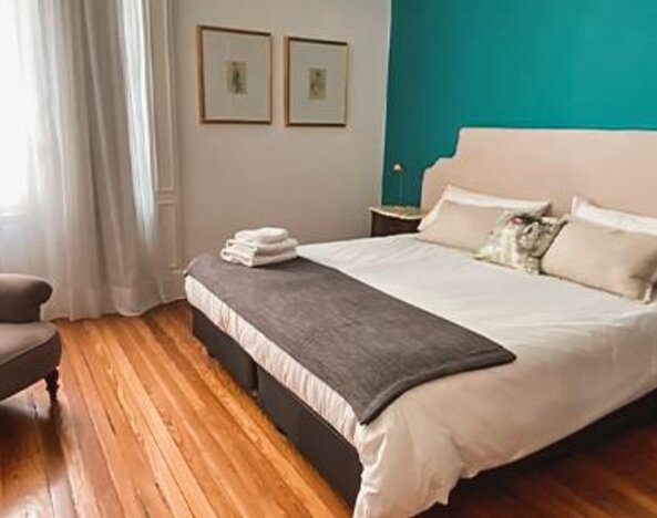 1. Guest bedroom with a king-size bed, teal accent wall, white bedding, grey throw and an armchair beside tall windows at Hotel Chemin.