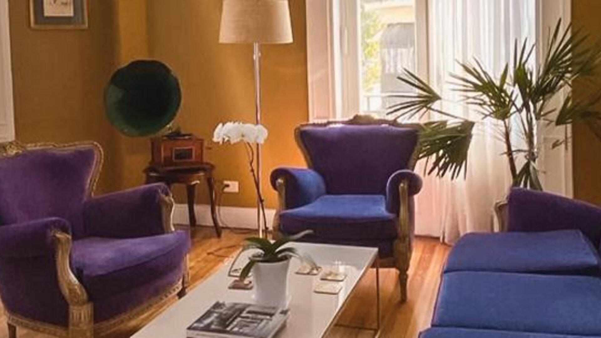 Lounge with purple upholstered sofas and armchairs, a white coffee table, wooden flooring and large windows at Hotel Chemin.