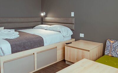 Compact studio with a bed, light wood furniture, upholstered headboard and a green accent chair with a patterned cushion at UMA Suites Chía.