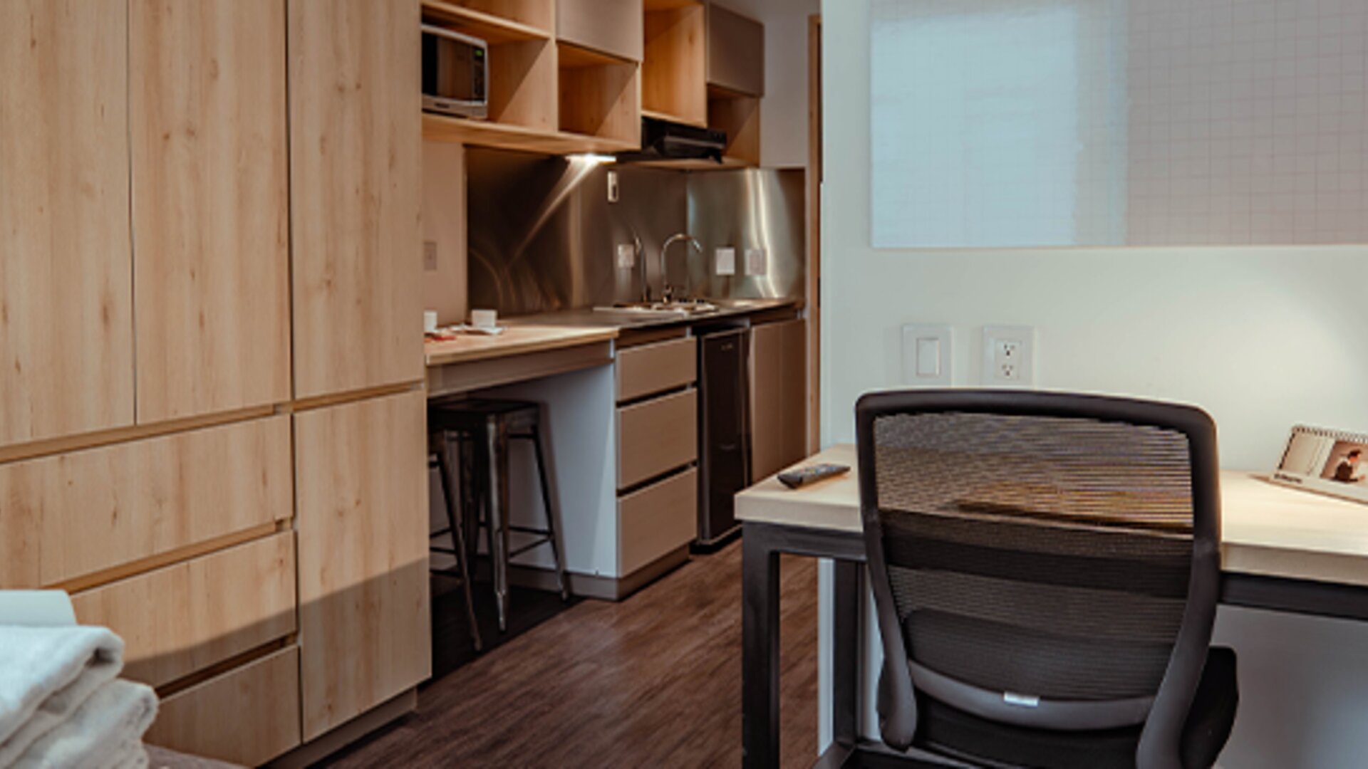 Studio interior with wooden cabinetry, a compact kitchenette, desk, office chair and dark wood-effect flooring at UMA Suites Chía.