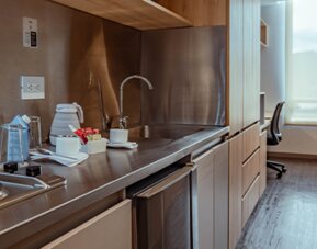Studio kitchenette with a two-burner electric hob, stainless-steel backsplash, sink, kettle and wooden cabinetry at UMA Suites Chía.