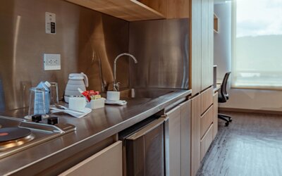 Studio kitchenette with a two-burner electric hob, stainless-steel backsplash, sink, kettle and wooden cabinetry at UMA Suites Chía.