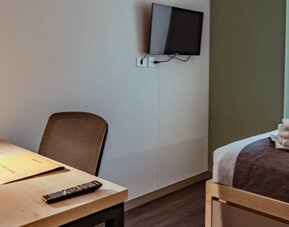 Compact guest room with a single bed, dark bed runner, wooden desk, chair and wall-mounted television at UMA Suites Chía.