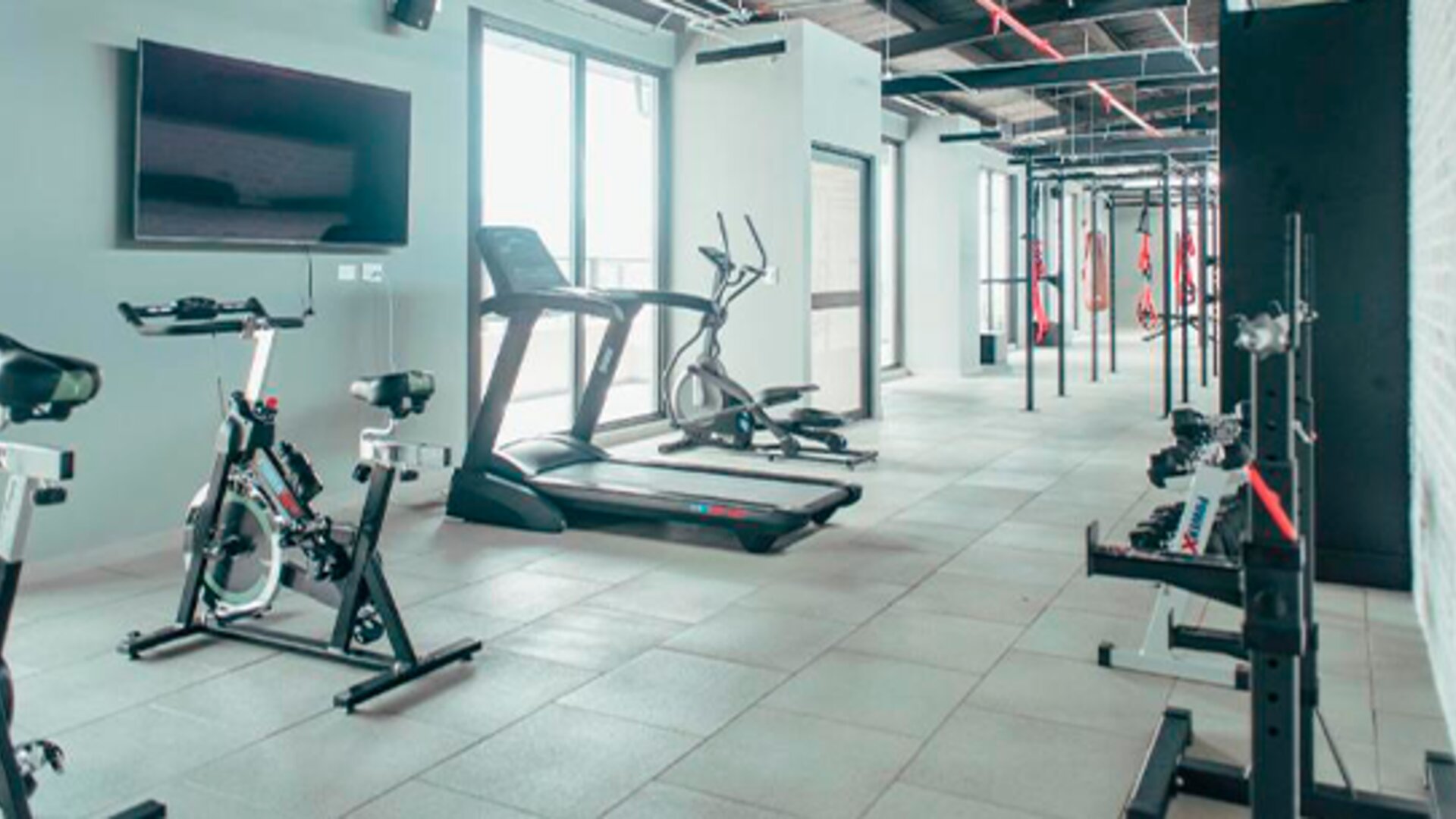 Fitness centre with stationary bikes, treadmills, strength equipment and a wall-mounted television at UMA Suites Chía.