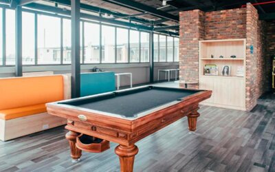 Games room with a wooden pool table, colourful booth seating, large windows and exposed brickwork at UMA Suites Chía.